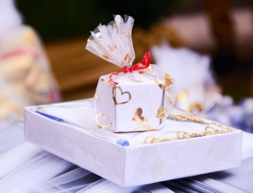 Una caja de regalo bellamente envuelta con corazones dorados y cinta roja, perfecta para ocasiones románticas.