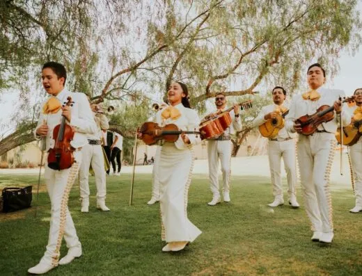 Una animada banda de mariachi en atuendo tradicional tocando al aire libre bajo los árboles.