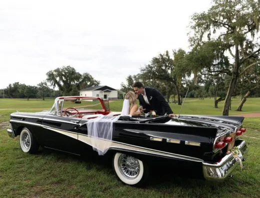 Recien casados besándose en un convertible clásico, disfrutando de un entorno al aire libre pintoresco.