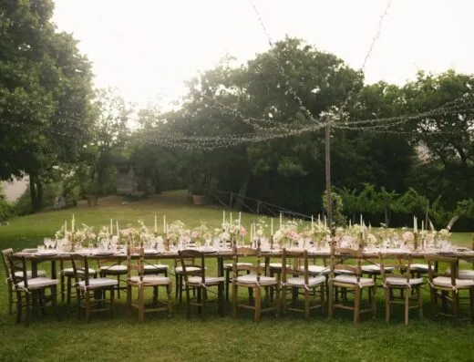 Hermosa mesa de recepción de boda al aire libre con decoraciones florales y luces colgantes en un jardín.