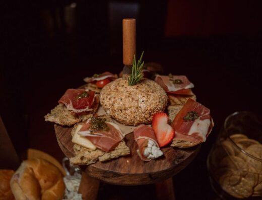 Un delicioso plato de quesos que incluye jamón, galletas y decorado con fresas.