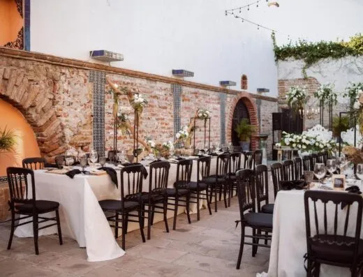 Elegante espacio de boda al aire libre con mesas, sillas y arreglos florales decorados.