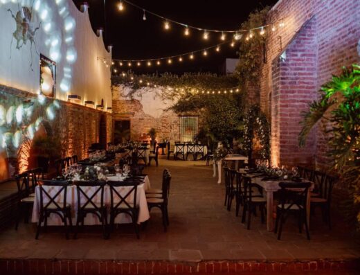 Encantador entorno para eventos al aire libre por la noche, con mesas con una decoración elegante bajo cálidas luces de cadena.
