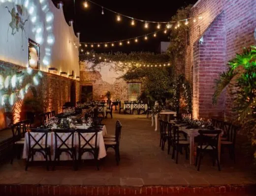 Encantador entorno para eventos al aire libre por la noche, con mesas con una decoración elegante bajo cálidas luces de cadena.