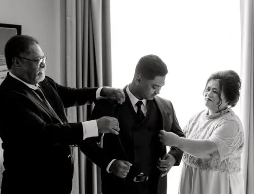 Una fotografía en blanco y negro que captura a un novio asistido por su familia antes de la ceremonia de la boda.