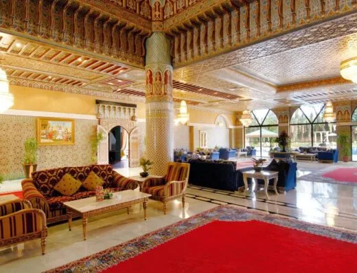 Lobby de hotel marroquí sofisticado con decoración ornamentada, asientos acolchados y candelabros.