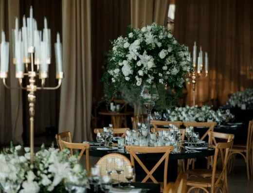 Configuración de recepción de boda de lujo con elegantes arreglos florales y mesas iluminadas con velas en un sofisticado lugar interior.