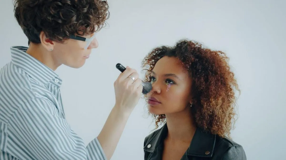 Una maquilladora aplica delicadamente colorete a una modelo con un maquillaje de ojos floral (imagen de referencia)