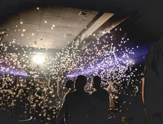 Escena enérgica de club nocturno con personas celebrando, confeti iluminado por focos creando una atmósfera dinámica.