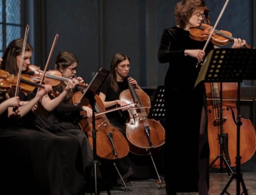 Un grupo de mujeres músicos interpretando música clásica con violines y cellos en un entorno orquestal.