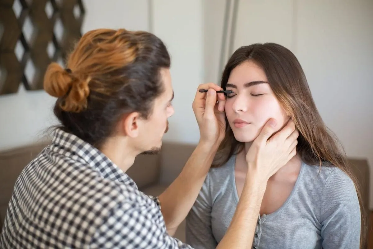 Un maquillador aplica maquillaje en los ojos de una mujer en interiores. Capturando la belleza y la artesanía en un entorno personal (imagen de referencia)