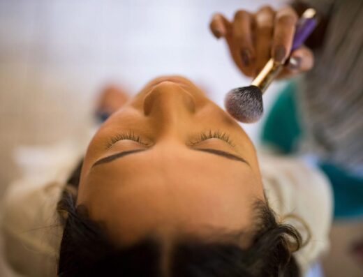 Vista en primer plano de un maquillador aplicando rubor con un pincel en el rostro de una mujer.