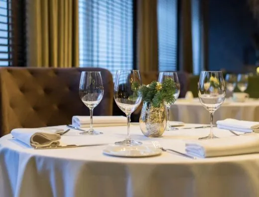 Configuración de comedor sofisticada con copas de vino pulidas, servilletas blancas y un centro de mesa decorativo en una mesa redonda.
