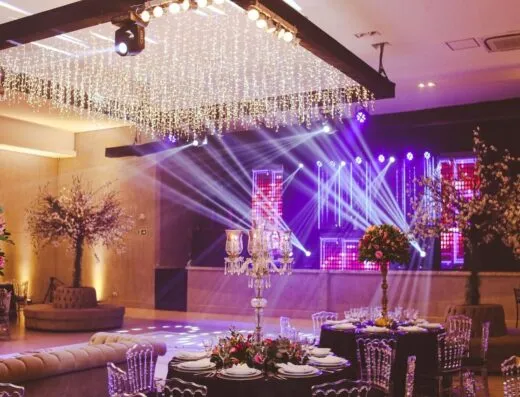 Impresionante montaje de salón decorado con candelabros de cristal, arreglos florales y vibrante iluminación en el escenario.