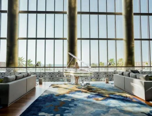Un vestíbulo de hotel moderno en Dubái con un piano de cola, sofás mullidos y grandes ventanas que ofrecen una vista impresionante.
