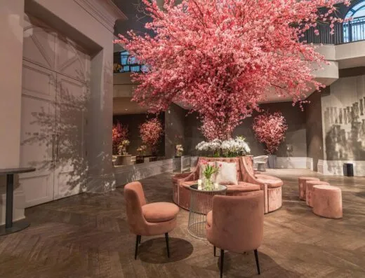 Lobby de hotel de lujo adornado con flores de cerezo rosas y un elegante arreglo de asientos.