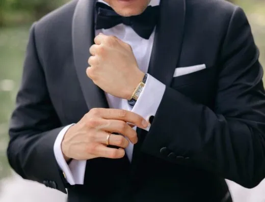 Primer plano de un hombre bien vestido ajustándose los gemelos, mostrando un reloj de pulsera dorado y un anillo de boda.
