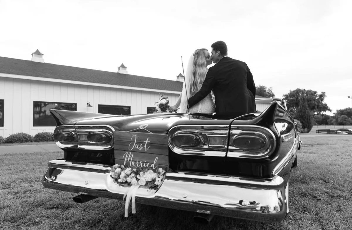 Los recién casados comparten un beso en un convertible clásico con un cartel de 'Recién Casados' (imagen de referencia)