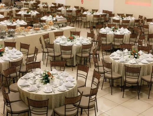 Amplia configuración de banquete con mesas redondas ordenadamente dispuestas y centros de mesa florales, lista para un gran evento.