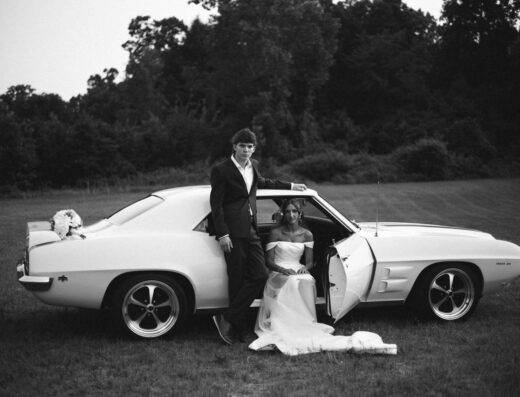 Foto en blanco y negro de una pareja con un coche clásico, capturando elegancia y estilo vintage.