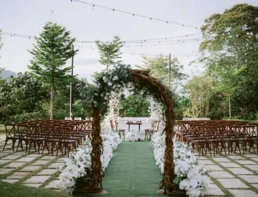 Hermoso montaje de ceremonia de boda al aire libre con arco, sillas y luces en un jardín exuberante.