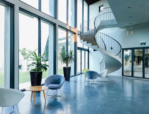 Lobby espacioso con escalera en espiral, grandes ventanas y zona de estar moderna.