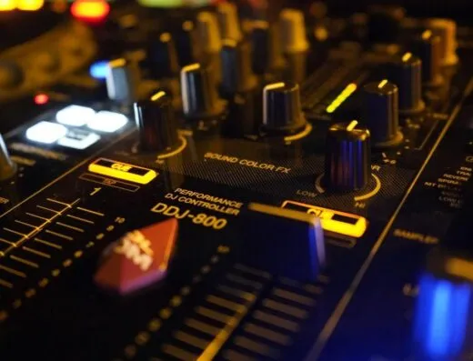 Un controlador de DJ con perillas y deslizadores iluminados, destacando equipos de audio técnico en iluminación tenue.