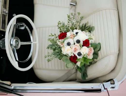 Un precioso arreglo floral con rosas y anémonas colocado en el interior del asiento de cuero blanco de un coche clásico.