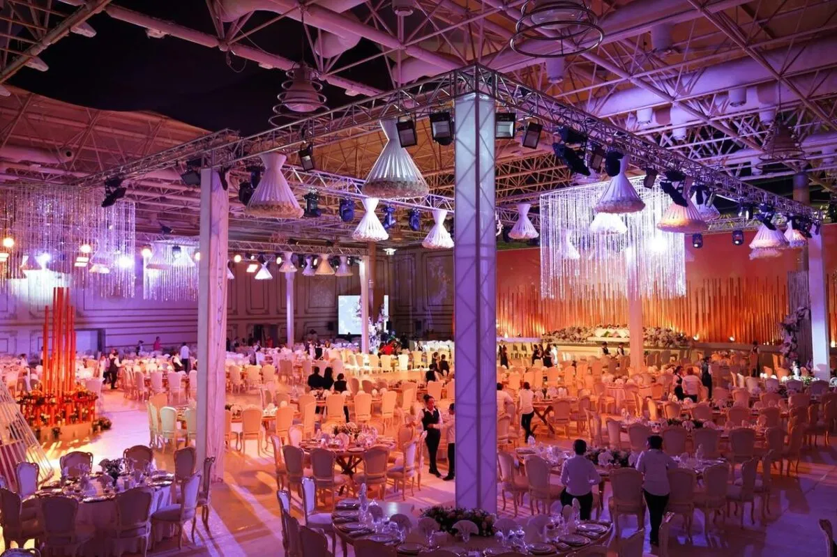 Una gran recepción de boda interior con iluminación ornamentada, mesas y una atmósfera vibrante (imagen de referencia)
