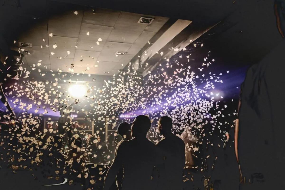 Escena enérgica de club nocturno con personas celebrando, confeti iluminado por focos creando una atmósfera dinámica (imagen de referencia)