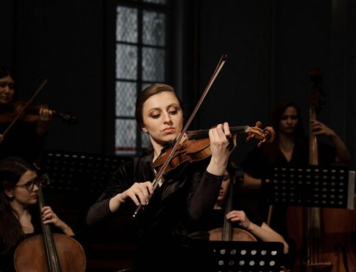 Una violinista toca apasionadamente en un entorno de orquesta clásica.