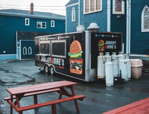 Un camión de comida estacionado al aire libre en un día lluvioso con un edificio azul al fondo.