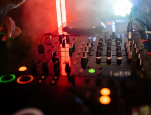 Primer plano dinámico de un mezclador de DJ en un ambiente de club nocturno con luces coloridas y una atmósfera envolvente.
