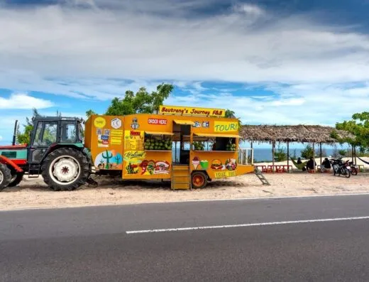 Camión de comida colorido en playa tropical con tractor, ofreciendo una escena vibrante.
