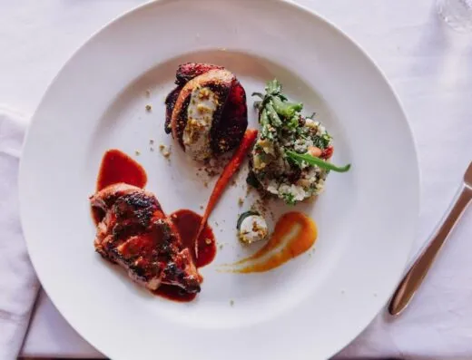 Elegante plato gourmet con carne a la parrilla y arreglo artístico de vegetales.