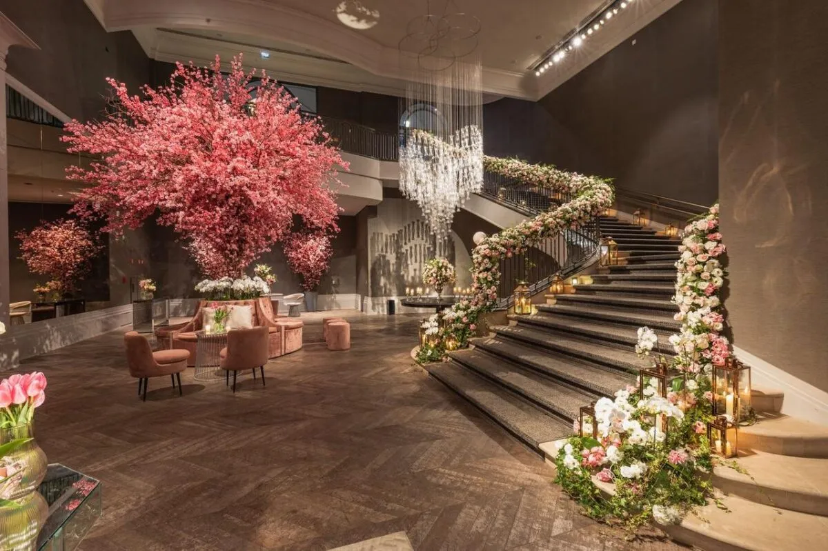 Un gran vestíbulo de hotel con exquisitas decoraciones florales, escalera de caracol y elegantes candelabros (imagen de referencia)