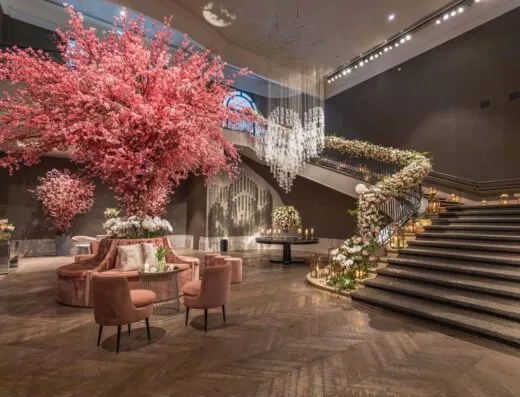 Lobby de hotel lujoso con grandes arreglos florales y escalera elegante.
