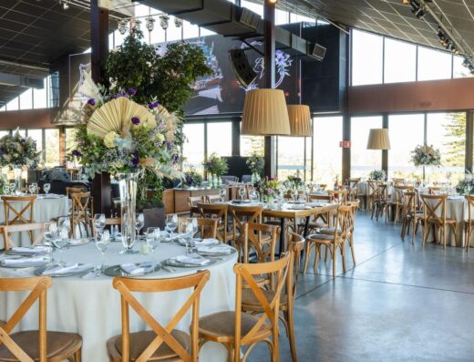 Un salón de recepción de bodas bellamente decorado con arreglos florales, iluminación elegante y mesas organizadas.