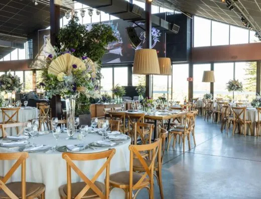 Un salón de recepción de bodas bellamente decorado con arreglos florales, iluminación elegante y mesas organizadas.
