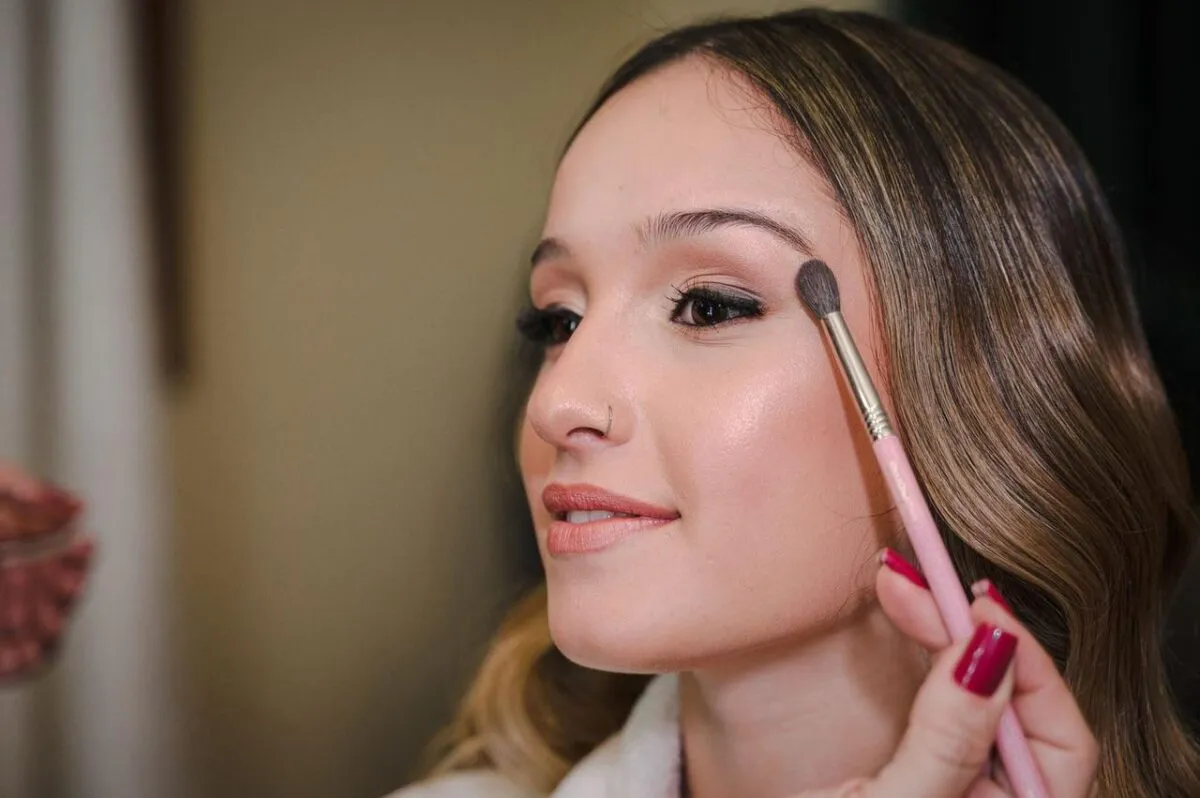 Primer plano de una mujer joven aplicando maquillaje con un pincel, mostrando belleza y elegancia (imagen de referencia)