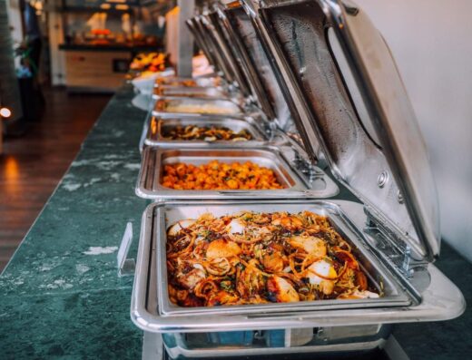 Una elegante disposición de buffet con varios platos deliciosos en bandejas de acero inoxidable, perfecto para eventos.