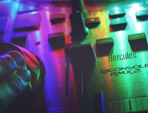 Primer plano de una consola de DJ bajo luces de neón coloridas, mostrando los controles y una mano ajustando los botones.