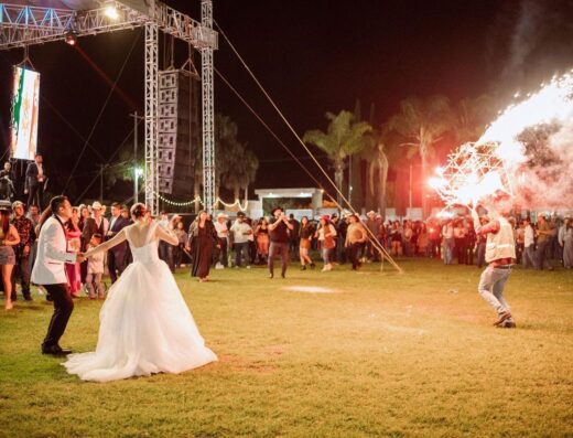 Una animada recepción de boda al aire libre con baile y fuegos artificiales bajo el cielo nocturno.