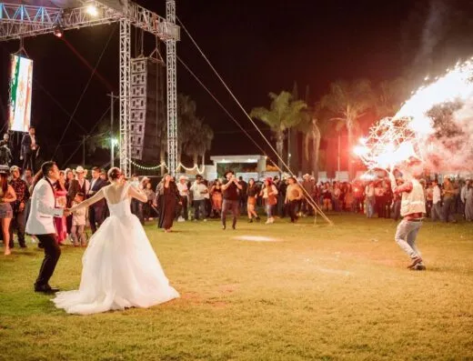 Una animada recepción de boda al aire libre con baile y fuegos artificiales bajo el cielo nocturno.