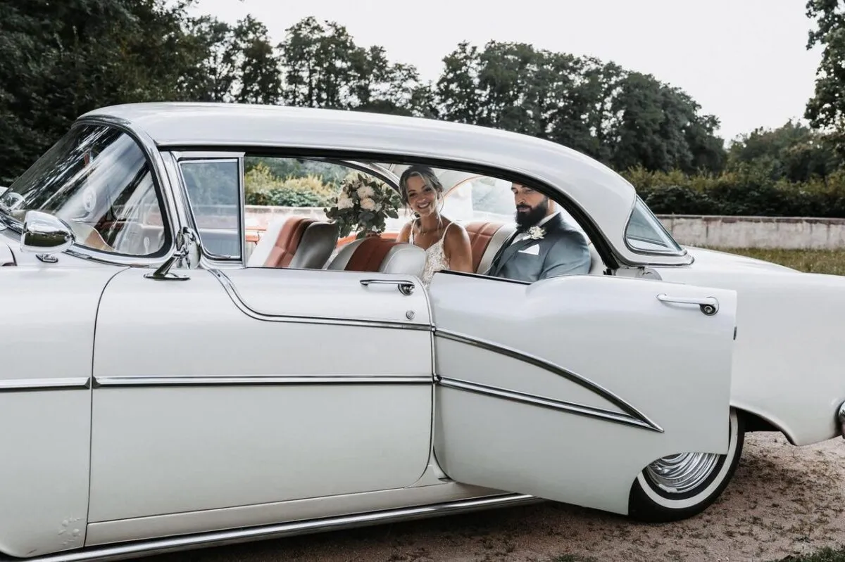 Pareja de novios en un coche blanco clásico, sonrientes y alegres en su día especial (imagen de referencia)
