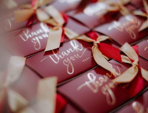 Un primer plano de cajas de regalo rojas bellamente envueltas con etiquetas de "Gracias" y cintas doradas.