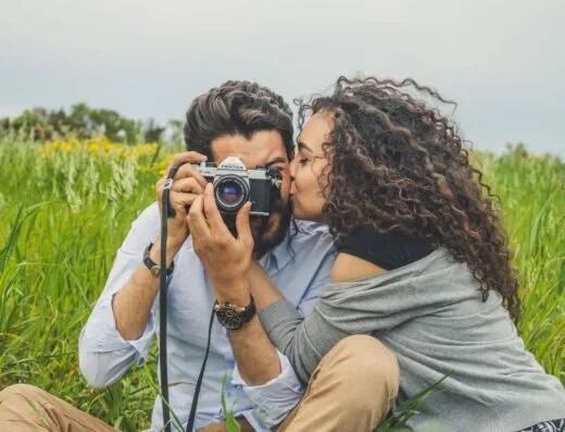 Pareja compartiendo un momento romántico con una cámara en un campo verde.