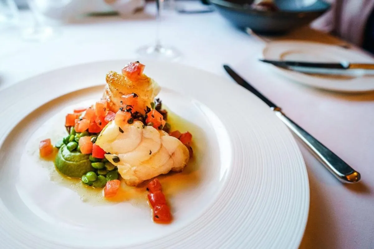 Elegante plato gourmet de pescado con guisantes y tomates, presentado de manera artística. Perfecto para entusiastas de la cocina (imagen de referencia)