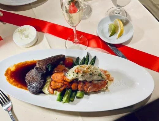 Elegante cena de surf and turf con filete, langosta y espárragos, acompañada de champán.