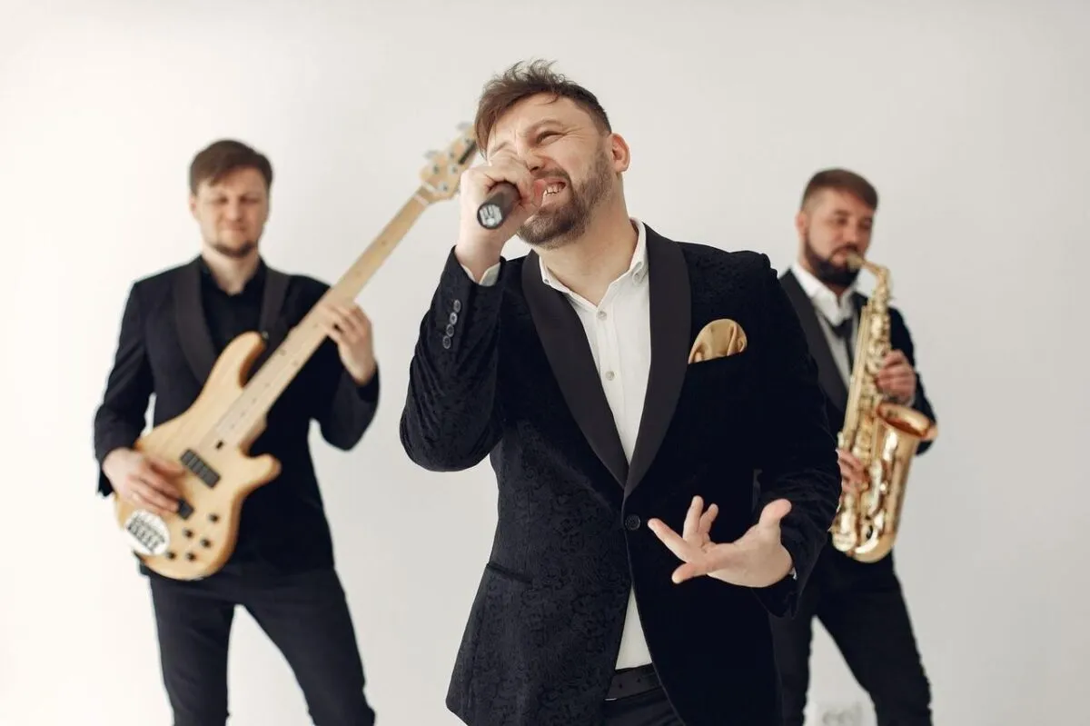 Actuación enérgica de banda en vivo con músicos tocando guitarra, saxofón y cantando en interiores (imagen de referencia)